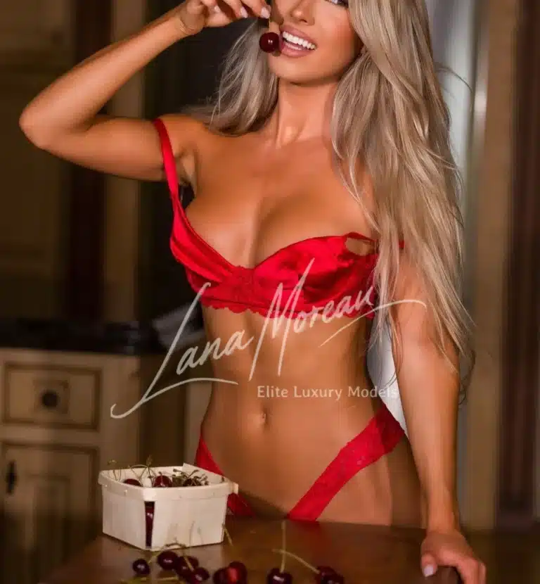 Charming Vera in red lingerie playfully posing with cherries, New York's irresistible blonde muse.